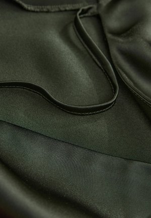 Ciemnozielony satynowy materiał o gładkiej fakturze, z wyraźnymi zakrzywionymi liniami i kontrastowymi matowymi obszarami, podkreślający płynny design i warstwowość.