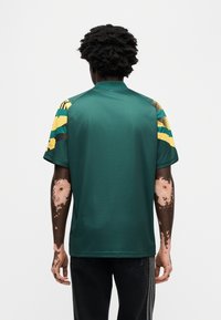 Πράσινο αθλητικό πουκάμισο με κίτρινες και μαύρες ριγέ κοντές μανίκες, με ψηλό γιακά και ομαλή υφή. Ορατή λεπτομέρεια ραφής.