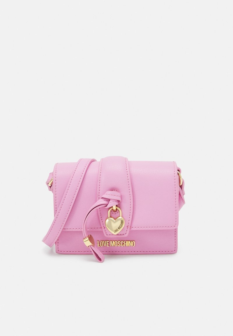Růžová syntetická kabelka s klopnou, zlatým srdíčkovým kováním a nastavitelným ramenním popruhem. Na přední straně se nachází logo.