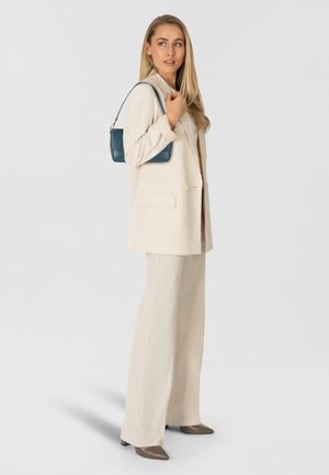 Conjunto de blazer y pantalones beige, combinado con un bolso color azul verdoso. Tejido suave, corte entallado, con bolsillos delanteros. Tacones puntiagudos marrones completan el look.