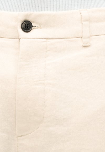 Κοντινό πλάνο της μέσης παντελονιού εκρού χρώματος με κουμπί κλεισίματος και θηλιά ζώνης, που δείχνει την υφή του υφάσματος και τις λεπτομέρειες της ραφή.