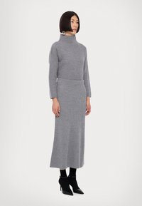 Grå strikket sweater og nederdel sæt med en mock neck, ribbet tekstur og sidelayout. Parret med sorte ankelstøvler og sokker.
