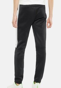 Schwarze Sportleggings mit schlankem Schnitt, ausgestattet mit weißen Seitestreifen und einer glatten Textur. Getragen mit weißen Schuhen.