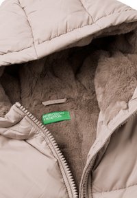 Beżowa pikowana kurtka z miękkim brązowym futrzanym podszyciem. Posiada kaptur, zamek błyskawiczny oraz zieloną metkę z napisem "United Colors of Benetton".