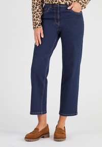 Jeans de mezclilla azul oscuro con un diseño de pierna recta, costuras en contraste y bolsillos frontales, combinados con mocasines de ante marrón.