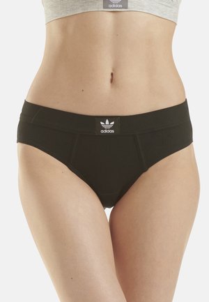 Female torso wearing black Adidas briefs and a grey Adidas crop top, showing branded logos on waistband and chest.