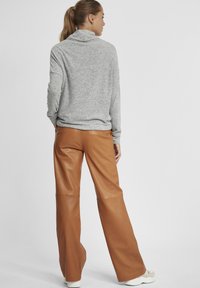 Maglione a collo alto grigio chiaro abbinato a pantaloni beige in pelle a vita alta e a gamba ampia. L'outfit presenta una texture morbida e una vestibilità rilassata.