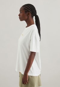 Hvid bomulds T-shirt med rund halsudskæring, korte ærmer, afslappet pasform og lille orange tekst trykt på forsiden.