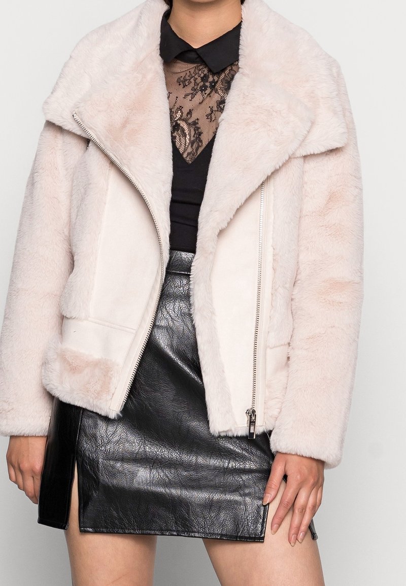 Femme portant une veste en fausse fourrure rose pâle sur un haut en dentelle noire et une mini-jupe en cuir noir avec une fente à l'avant.