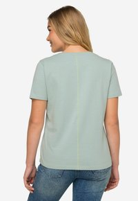 Camiseta de manga corta verde claro con escote redondo, que presenta una costura vertical prominente en la parte trasera y costuras contrastantes en amarillo.