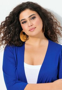 Cardigan azul con un diseño de escote en V, combinado con una blusa blanca. El modelo tiene el cabello rizado y lleva grandes pendientes de aro dorados.