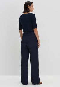 Marineblauwe jumpsuit met korte mouwen, brede benen, elastische taille en een gladde textuur. Eenvoudig ontwerp met minimale detailing.