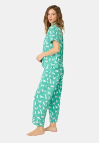 Grönt pyjamasset som består av en kortärmad topp och byxor, båda prydda med ett mönster av rosa och vita djur. Mjukt tyg, avslappnad passform.