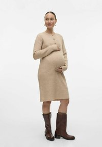 Robe en tricot beige avec une texture côtelée, des boutons sur le devant et des manches longues, associée à des bottes brunes montant jusqu'au genou avec des revers repliés.