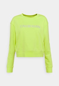 Limonkowy krótki sweter wykonany z miękkiego materiału. Posiada okrągły dekolt i długie rękawy, na których widnieje napis "CALVIN KLEIN" w jasnofioletowym kolorze.