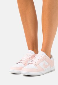 White and pink athletic sneakers with perforated toe box, textured leather, and rubber outsole. Laces and logo in contrasting colors.