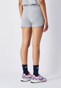 Graue Baumwollshorts mit hoher Taille, glatter Textur und einfachem Design. Kombiniert mit dunkelblauen Socken und sportlichen Sneakers.