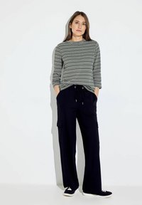 Multikleuren gestreepte lange mouwen shirt gecombineerd met zwarte wijde broek met zijzakken en een verstelbare trekkoord. Casual sneakers inbegrepen.