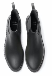 Un paio di stivali neri in gomma fino alla caviglia con linguette per il tallone e suole testurizzate, visti dall'alto su uno sfondo bianco.