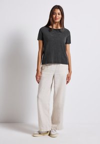 Gray short-sleeve t-shirt with a round neckline, featuring embossed text. Paired with loose, cream-colored linen pants and light sneakers.
