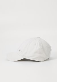 Fehér Nike baseball sapka ívelt csúccsal és kis ezüst swoosh logóval elöl, sima fehér háttér előtt bemutatva.