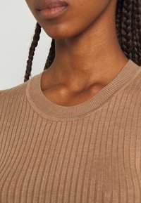 Haut en tricot côtelé marron avec un col rond, présentant une texture douce et un éclat subtil, très près du corps pour mettre en valeur le col et la zone du cou.