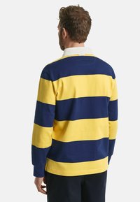 Langarm-Polohemd mit horizontalen Streifen in Marineblau und Gelb, einem weißen Kragen und einem geraden Saum aus strukturiertem Stoff.