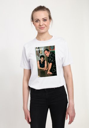 Bílý tričko s obdélníkovou grafikou dvou mužů u stolu, s nápisem "Sopranos" umístěným nad obrázkem, na světlém pozadí.