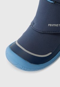 Nahaufnahme eines Kinderschneestiefels in Marineblau und Hellblau mit reflektierendem Streifen und strukturiertem Sohlen.