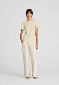 Light beige short-sleeve knit sweater paired with loose beige trousers. The fabric appears soft with a relaxed fit and rolled cuffs.