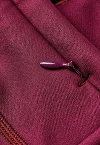 Gros plan d'une veste en tissu bordeau avec une fermeture éclair assortie partiellement fermée et un tissage texturé visible.