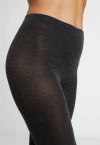 Czarne legginsy o miękkiej, prążkowanej teksturze i elastycznym pasie, dopasowane i zwężające się przy kostce. W niektórych miejscach lekko przezroczyste.