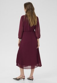 Rochie midi plisată în nuanță burgundy, cu mâneci lungi transparente și talie ajustată. Asortată cu pantofi cu toc slingback cu imprimeu zebra alb-negru.