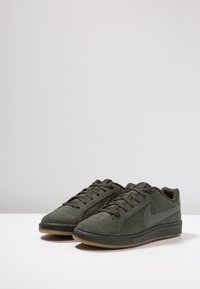 Zelené semišové tenisky s hladkým povrchem, kulatou špičkou a gumovou podrážkou. Mají texturovanou boční část a podpisové logo swoosh v šedé barvě.