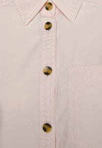 Camicia button-up rosa chiaro con colletto classico, sei bottoni rotondi di colori a contrasto e una tasca sul petto.