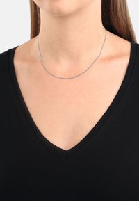 Collana in argento con un design delicato e liscio che poggia su un collo nudo, abbinata a una maglietta nera a V.
