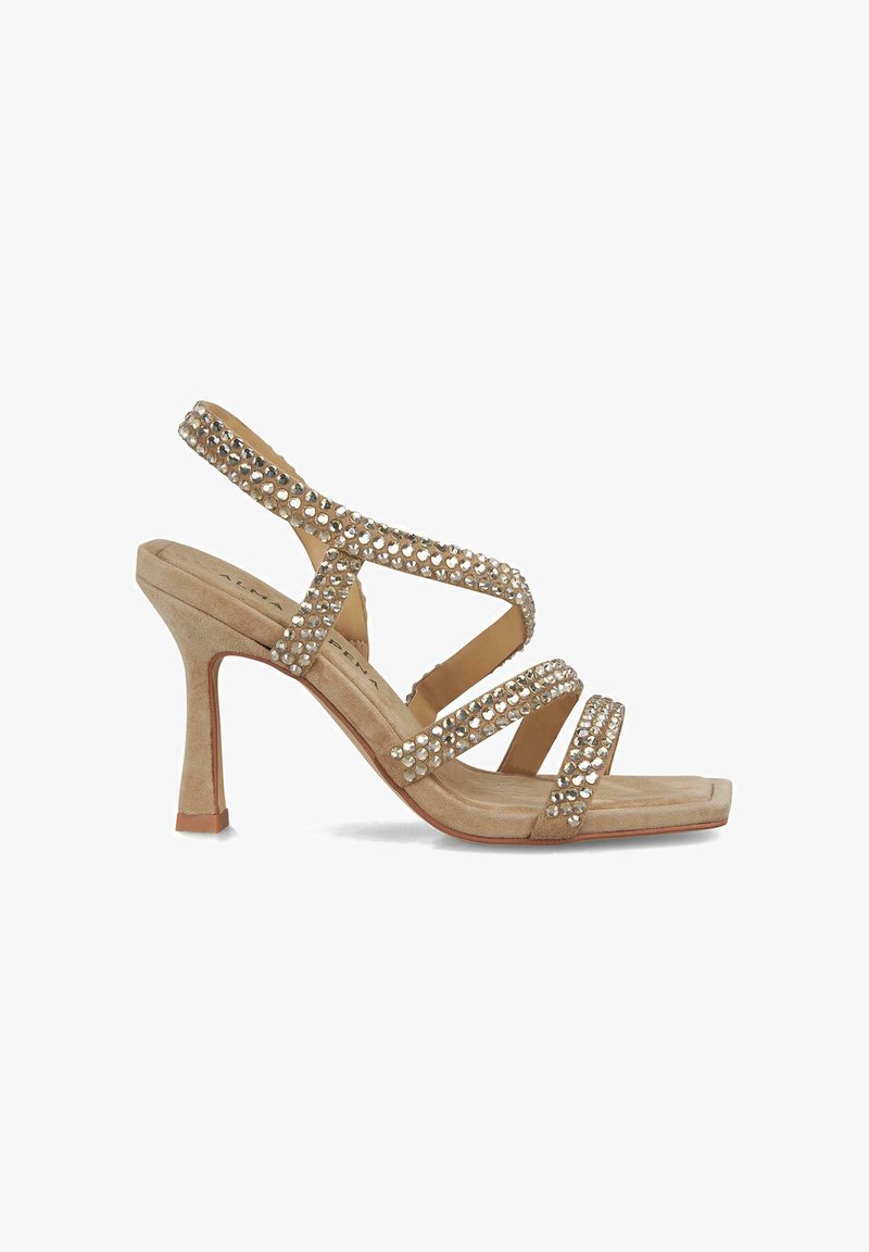 Sandale à talons hauts beige avec des brides entrecroisées, ornée de strass transparents. Texture en daim et design à bout carré.