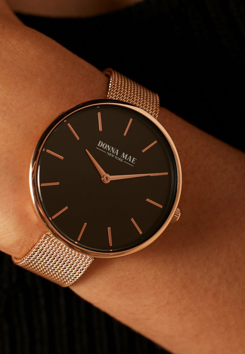 Schwarze Uhr mit glattem Zifferblatt, roségoldenen Zeigern und Markierungen, Mesh-Armband und dem Markennamen "DONNA MAE NEW YORK" deutlich sichtbar.