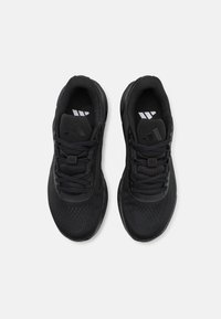 Baskets de sport noires avec une tige en mesh texturé, semelle en caoutchouc robuste et lacets noirs. Présentent un logo sur la languette et un design épuré.