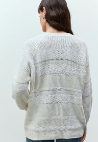 Pull en tricot gris clair avec des rayures texturées et des motifs à mailles ouvertes. Dispose de manches longues et d'une coupe décontractée.