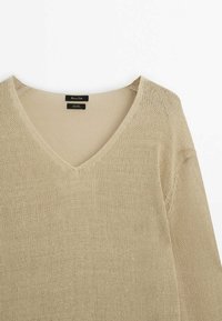 Beige neulepusero, jossa on V-pääntie, löysä malli ja pitkät hihat. Valmistettu kevyestä, teksturoidusta kankaasta. Tagi näkyvissä kauluksessa.