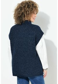 Maglione lavorato a maglia blu navy con collo alto e maniche corte, caratterizzato da un tessuto testurizzato e una vestibilità comoda, indossato sopra una camicia bianca.