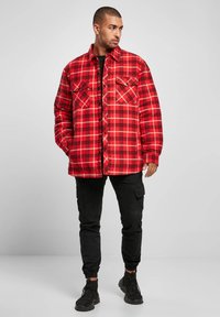 Red and black plaid flannel shirt with two chest pockets and button closure, paired with black cargo pants and black sneakers.