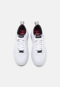 Sneakers bianchi con superficie testurizzata, dotati di lacci neri e logo, accenti rossi sulla linguetta e un alette per il tallone.