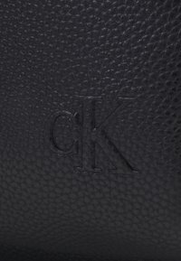 Pelle nera testurizzata con logo "CK" in rilievo, che presenta una superficie delicatamente stampata con una finitura morbida.