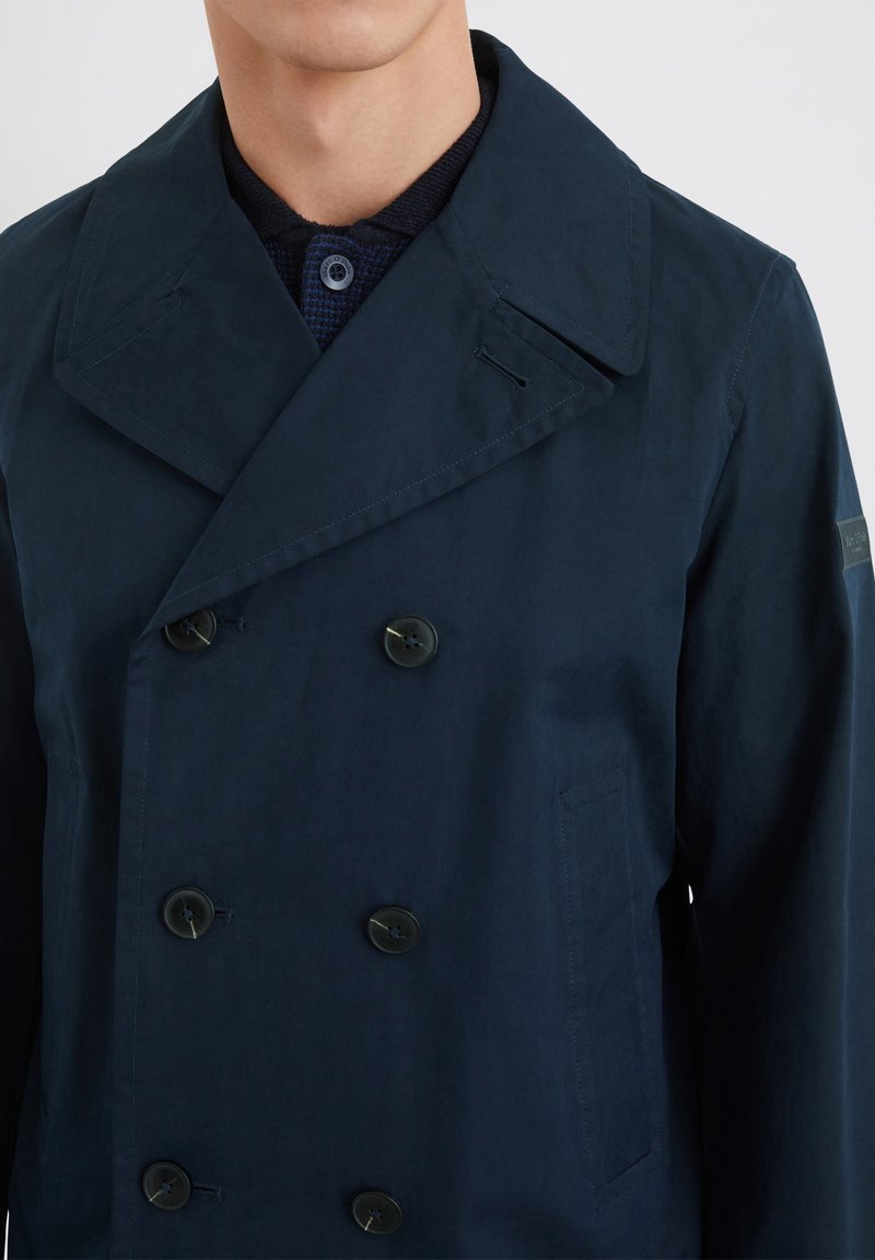 Marineblaue Doppelreiherjacke mit großem Kragen, strukturiertem Stoff und schwarzen Knöpfen sowie seitlichen Taschen.