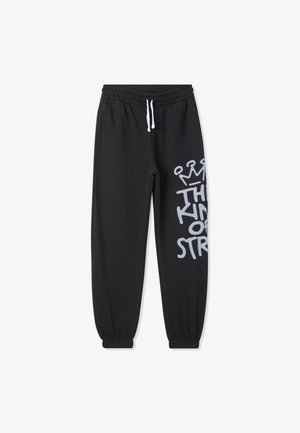 Pantaloni sportivi neri con vita elastica e coulisse, caratterizzati da una grande stampa grafica grigia sui lati. Polsini alle caviglie.