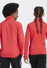 Veste en polaire de couleur corail vif avec un col montant, des manches longues et une texture lisse. Présente un bord contrastant le long des bras.