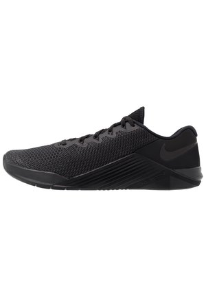 Zwart sportief schoen met een gestructureerd mesh bovenwerk, platte veters en een dikke rubberen zool met opvallende zijdelingse accenten.