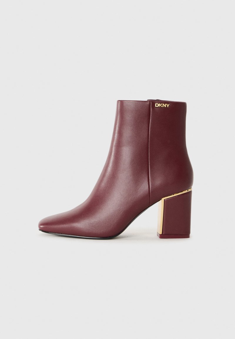 Botine din piele burgundă cu toc bloc și accent de aur, fermoar lateral și mic logo "DKNY" aproape de vârf.
